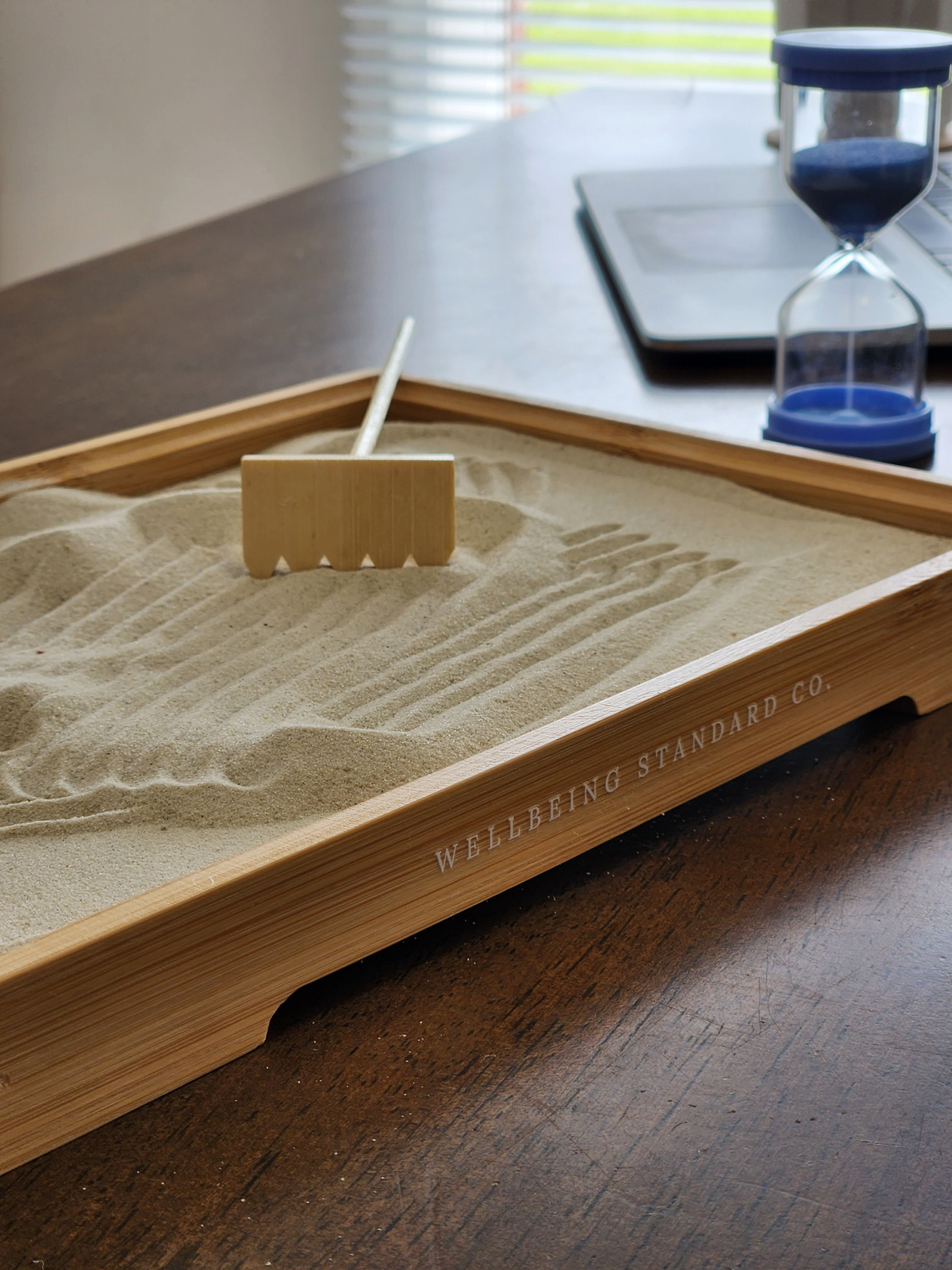 The Resetter sand tray with wooden rake and glass timer on a desk
